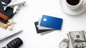 Credit cards on a white table with travel items, car keys, cash, a watch, a pen and a cup of coffee.